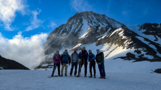 Life Happens Outdoors trekkers standing on snow beneath a steep alpine peak during a high altitude preparation climb.