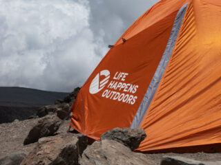 Orange Life Happens Outdoors tent at a high altitude camp on Kilimanjaro under cloudy skies