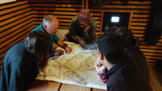 Mountain guide briefing trekkers over a route map before a Life Happens Outdoors adventure