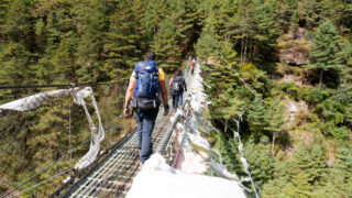 Trekkers crossing a suspension bridge in Nepal while planning a mountain adventure with Life Happens Outdoors