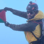 Close-up of Adel Nazih holding the Palestinian flag on the Eiger summit after his 16 July 2026 ascent with LHO.