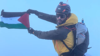 Close-up of Adel Nazih holding the Palestinian flag on the Eiger summit after his 16 July 2026 ascent with LHO.