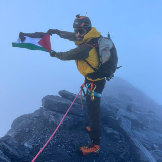 del Nazih holding the Palestinian flag on the rocky summit of the Eiger after climbing the Mittellegi Ridge with LHO.