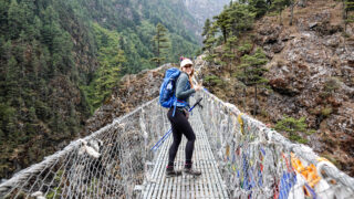 Trekker crossing a suspension bridge on the lower trail shared by the Everest Base Camp and Gokyo Lakes routes in Nepal.