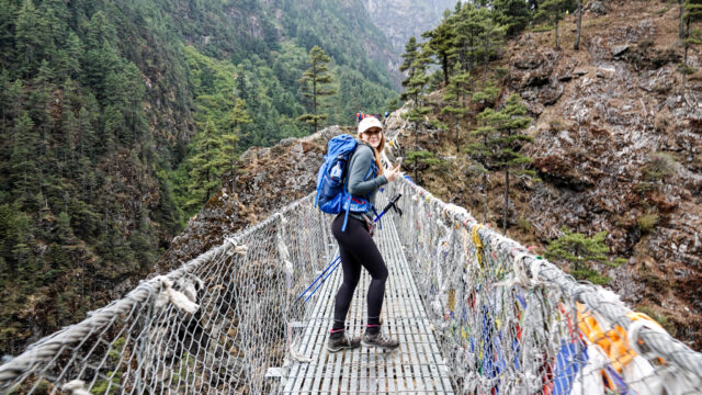 Trekker crossing a suspension bridge on the lower trail shared by the Everest Base Camp and Gokyo Lakes routes in Nepal.