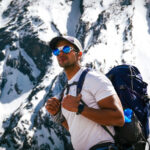 Trekker carrying a backpack beneath snowy mountain peaks during a high altitude acclimatisation hike