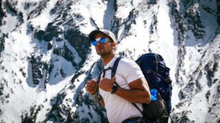 Trekker carrying a backpack beneath snowy mountain peaks during a high altitude acclimatisation hike