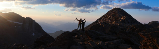 Three Life Happens Outdoors adventurers standing together on a rocky mountain ridge at sunrise.