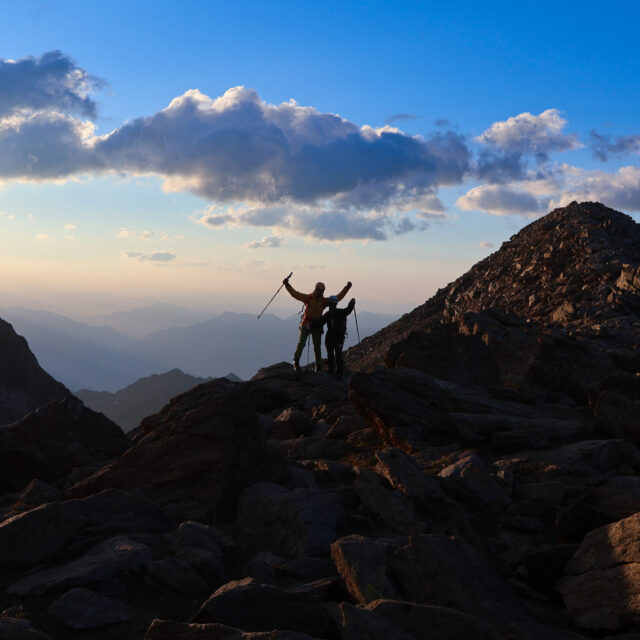 Three Life Happens Outdoors adventurers celebrating together on a rocky mountain ridge at sunrise.