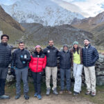 Life Happens Outdoors trekkers at a high altitude mountain camp beneath snow covered peaks.