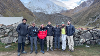 Life Happens Outdoors trekkers at a high altitude mountain camp beneath snow covered peaks.