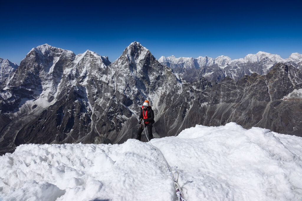 Climber on a snowy ridge during a Lobuche East climb with Himalayan peaks in the background