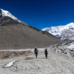 Two trekkers walking from Chukhung towards Island Peak Base Camp beneath snow covered Himalayan peaks