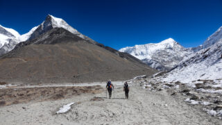 Two trekkers walking from Chukhung towards Island Peak Base Camp beneath snow covered Himalayan peaks