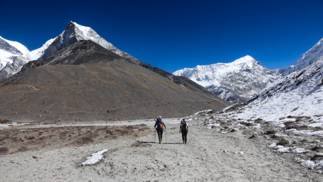 Two trekkers walking from Chukhung towards Island Peak Base Camp beneath snow covered Himalayan peaks