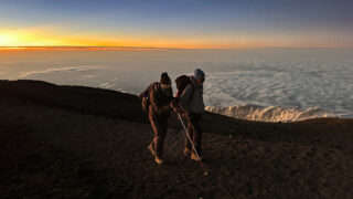 Fred Sfeir supported by a Life Happens Outdoors guide moving together above the clouds at sunrise during the Moving Mountains Kilimanjaro ascent.