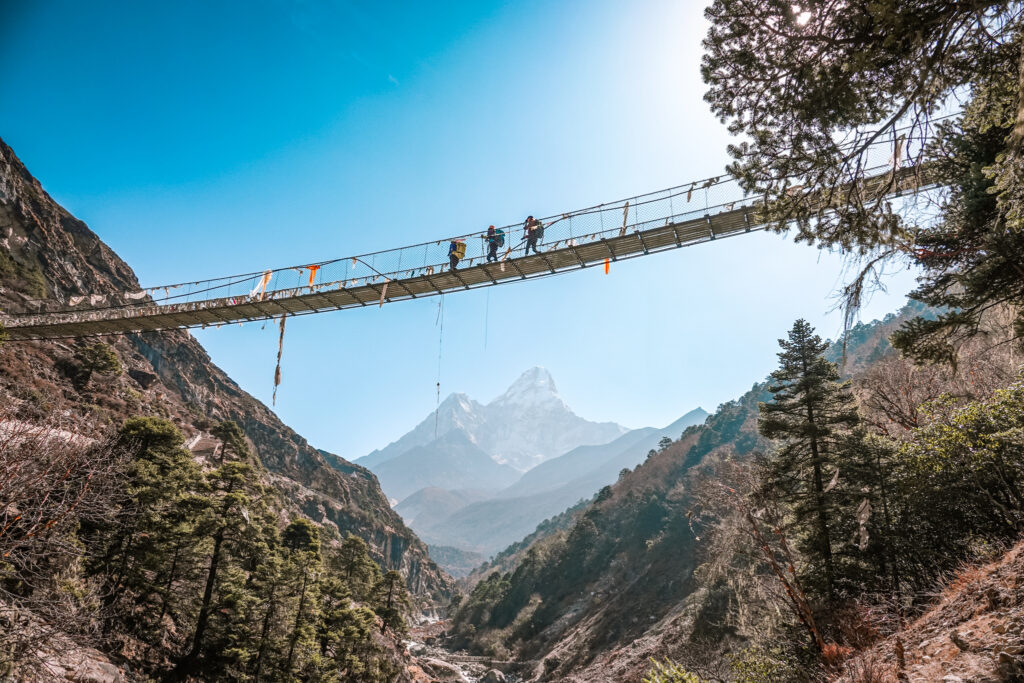 Trekkers crossing a suspension bridge with Ama Dablam visible on the shared trail towards Namche Bazaar