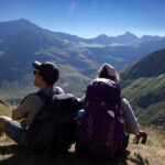 Two hikers resting above an alpine valley while trekking in the Alps