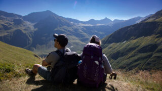Two hikers resting above an alpine valley while trekking in the Alps