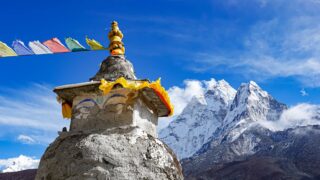 Buddhist chorten and prayer flags beneath snow-covered Himalayan peaks in Nepal.
