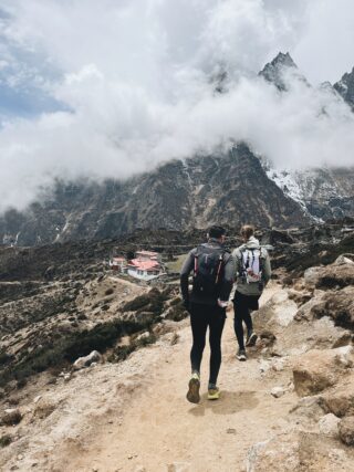 Two people following a rocky trail beneath Himalayan mountains.