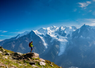 Life Happens Outdoors trekker with walking poles overlooking snow covered mountains.